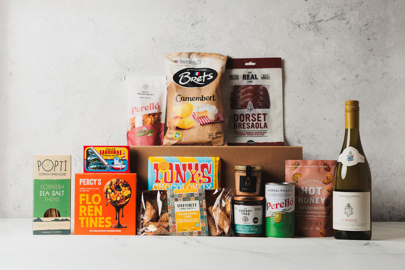 Assorted food products including snacks, a bottle of wine, and boxes on a gray surface.