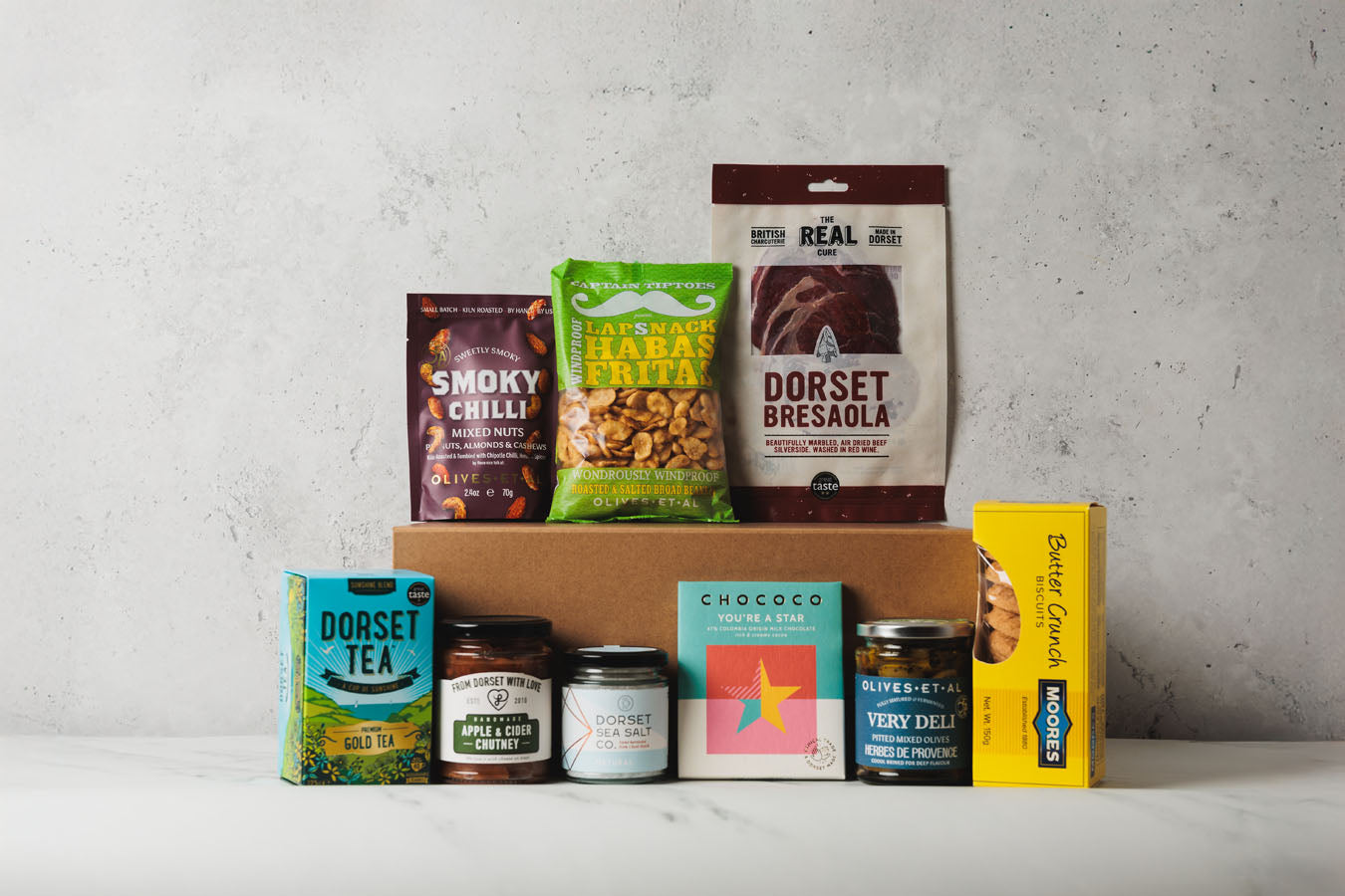 Collection of food products including Dorset Tea, Smoky Chilli, and Dorset Bresaola in a box on a gray background.