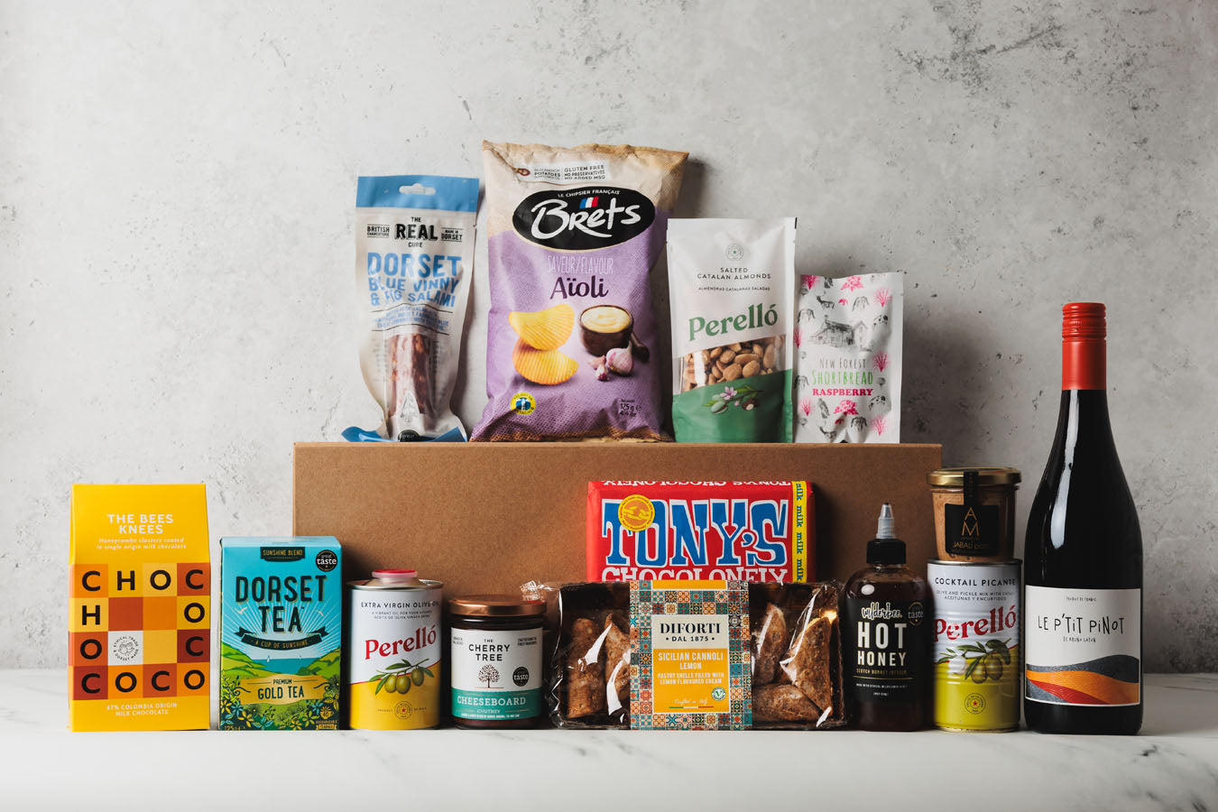 Assorted groceries including snacks, tea, and wine on a gray surface with a neutral background.